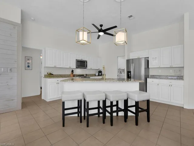 Kitchen with a ceiling fan, white cabinets, a kitchen bar, an island with sink, and stainless steel appliances