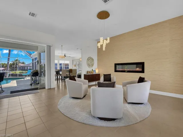 Living area with a sunroom, ceiling fan, an accent wall, a glass covered fireplace, and light tile patterned floors