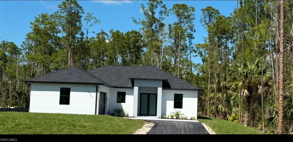 View of front of home with a shingled roof, a front yard, a forest view, and stucco siding