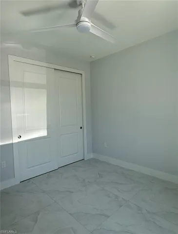 Unfurnished bedroom featuring marble finish floor, a ceiling fan, baseboards, and a closet