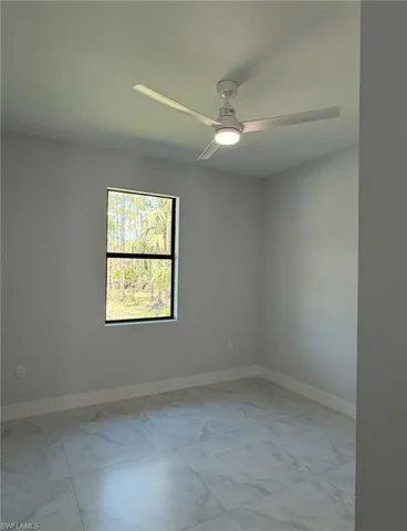 Unfurnished room featuring marble finish floor, a ceiling fan, and baseboards
