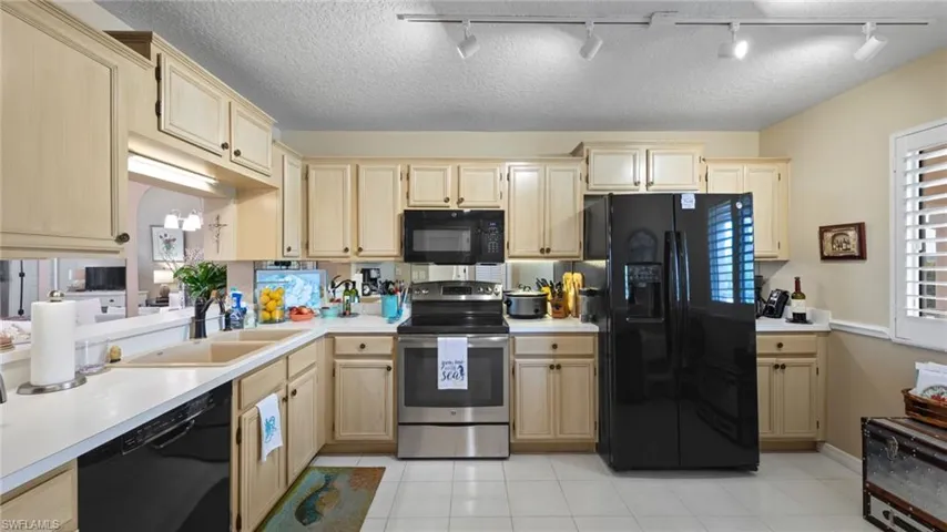 Kitchen with black appliances, rail lighting, a sink, light brown cabinets, and light countertops