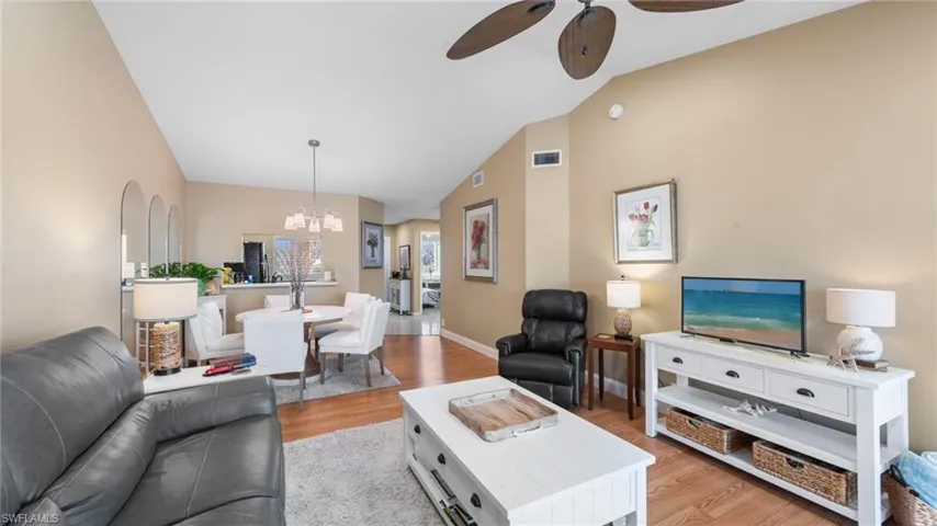 Living area featuring ceiling fan, a chandelier, lofted ceiling, light wood-style flooring, and baseboards