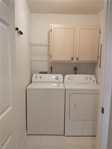 Laundry area with cabinet space, washing machine and dryer, light tile patterned floors, and a textured ceiling