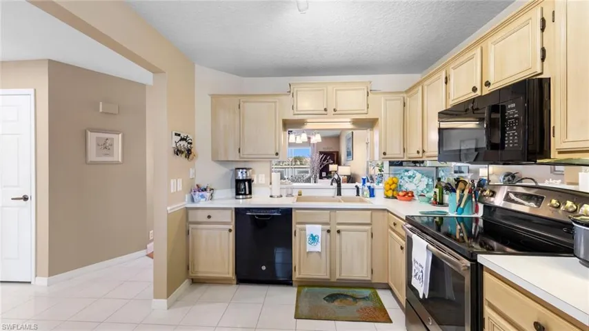Kitchen featuring black appliances, a sink, light brown cabinetry, light countertops, and a textured ceiling