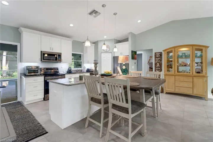Kitchen with appliances with stainless steel finishes, white cabinetry, vaulted ceiling, pendant lighting, and a center island