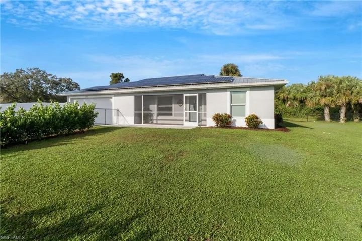 Rear view of house featuring a sunroom, a lawn, and solar panels