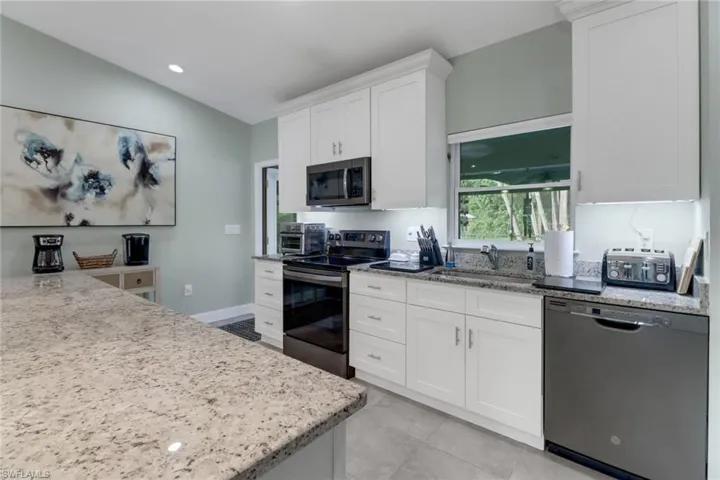 Kitchen with white cabinetry, stainless steel appliances, lofted ceiling, and sink