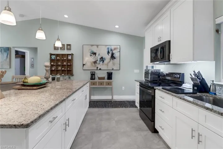 Kitchen featuring light stone countertops, black appliances, lofted ceiling, decorative light fixtures, and white cabinets