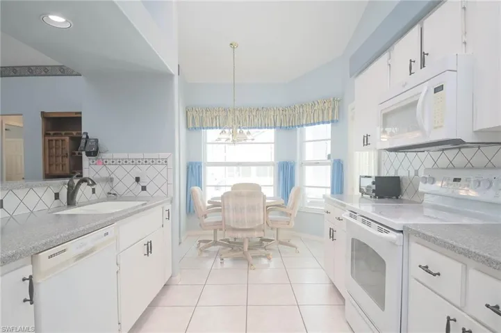 Kitchen featuring white cabinetry, tasteful backsplash, white appliances, sink, and an inviting chandelier