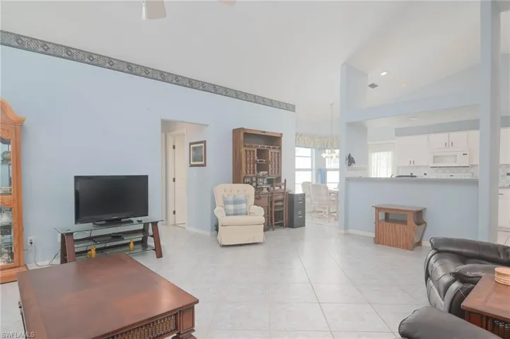 Living room with ceiling fan with notable chandelier, light tile patterned floors, and high vaulted ceiling
