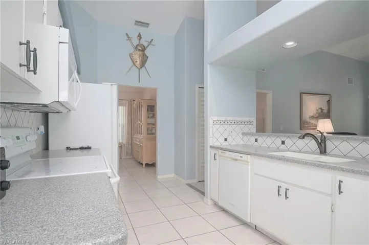 Kitchen with decorative backsplash, white appliances, sink, and white cabinets