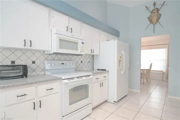 Kitchen featuring white cabinets, tasteful backsplash, light tile patterned flooring, and white appliances