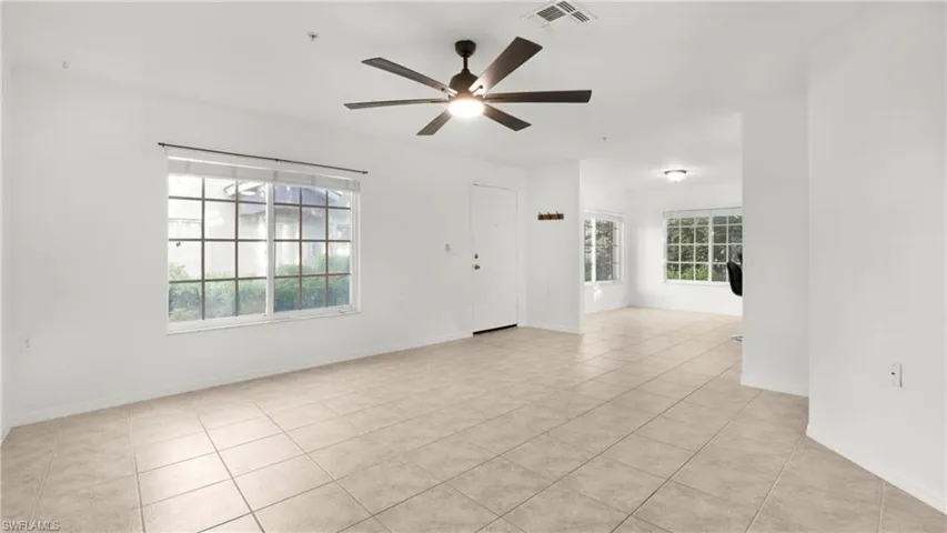 Empty room with light tile patterned floors, healthy amount of natural light, and a ceiling fan