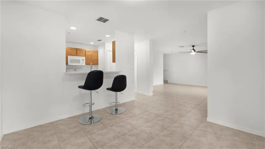 Kitchen featuring a kitchen breakfast bar, recessed lighting, light tile patterned floors, white microwave, and ceiling fan