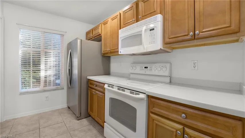 Kitchen with white appliances, light countertops, light tile patterned floors, and brown cabinetry