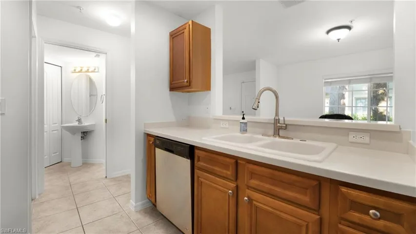Kitchen featuring stainless steel dishwasher, brown cabinetry, light countertops, and light tile patterned flooring