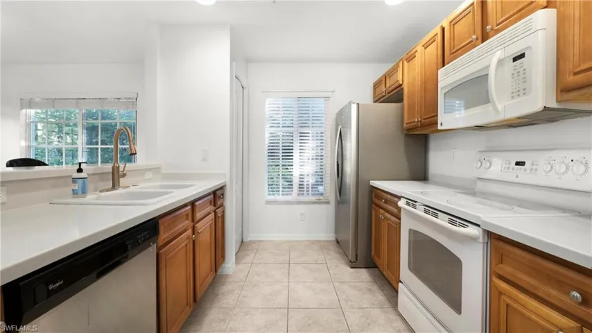 Kitchen with white appliances, light tile patterned floors, brown cabinetry, light countertops, and recessed lighting