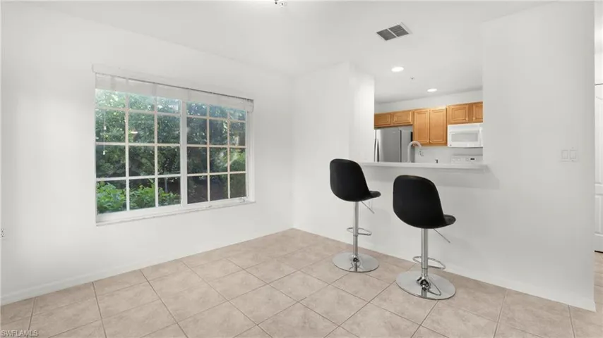 Kitchen with a breakfast bar, recessed lighting, light tile patterned floors, freestanding refrigerator, and white microwave