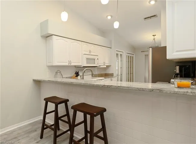 Kitchen featuring white cabinets, pendant lighting, lofted ceiling, light stone countertops, and white appliances