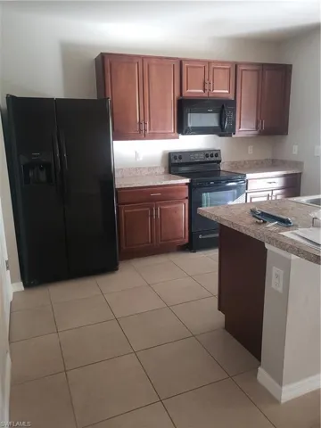 Kitchen featuring black refrigerator, range, light tile patterned floors, and light countertops