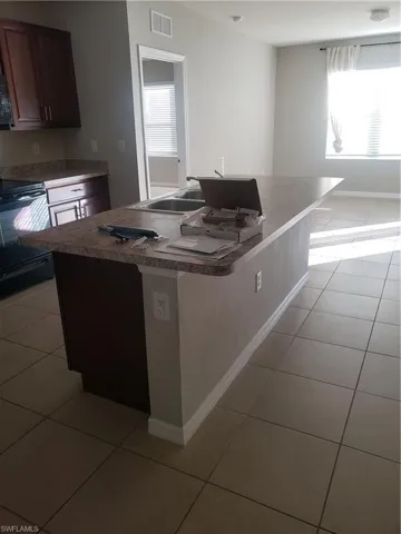 Kitchen with light tile patterned flooring, range, a kitchen island with sink, and white microwave