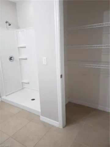 Full bathroom with a shower stall, light tile patterned floors, and a closet