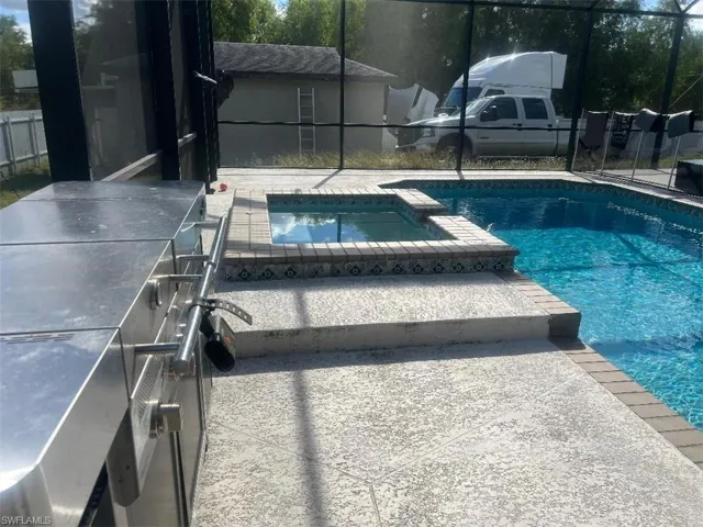 Combined pool / hot tub with a grill, a patio area, and glass enclosure