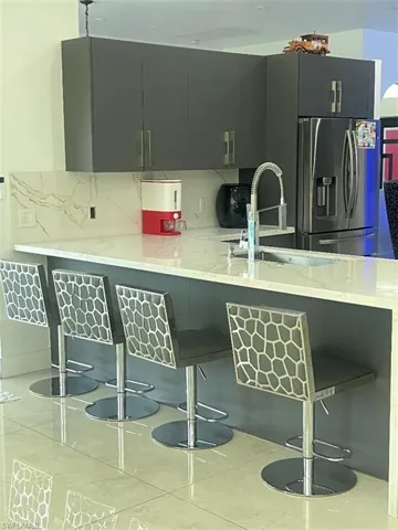 Kitchen featuring a breakfast bar area, light stone countertops, stainless steel fridge with ice dispenser, and gray cabinets