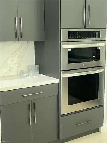 Kitchen featuring double oven, tasteful backsplash, and gray cabinetry