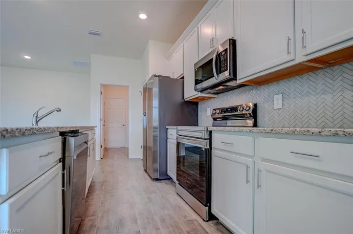 Kitchen featuring white cabinets, light hardwood / wood-style flooring, decorative backsplash, light stone counters, and stainless steel appliances