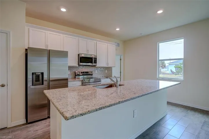 Kitchen with appliances with stainless steel finishes, light stone counters, a kitchen island with sink, sink, and white cabinets