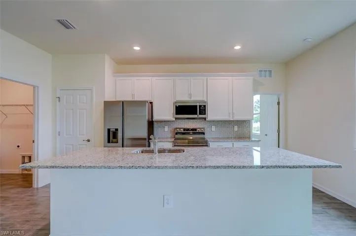 Kitchen featuring stainless steel appliances, white cabinetry, a center island with sink, and sink
