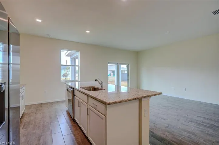 Kitchen with light stone countertops, appliances with stainless steel finishes, a kitchen island with sink, sink, and light hardwood / wood-style flooring