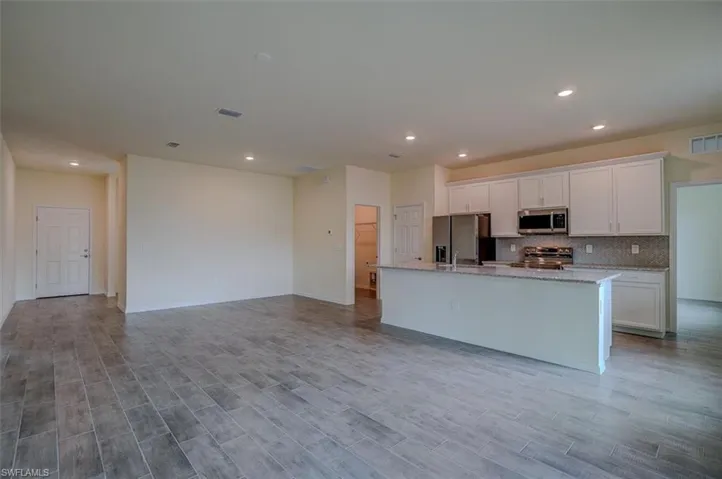Kitchen featuring white cabinets, light wood-type flooring, an island with sink, and appliances with stainless steel finishes