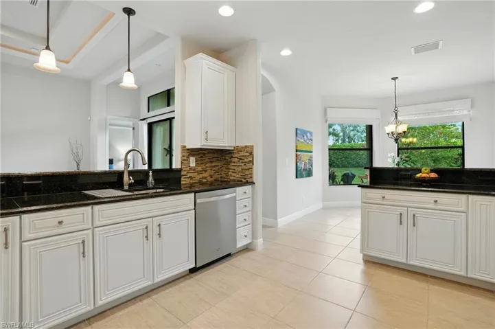 Kitchen featuring dishwasher, backsplash, pendant lighting, white cabinetry, and dark stone countertops