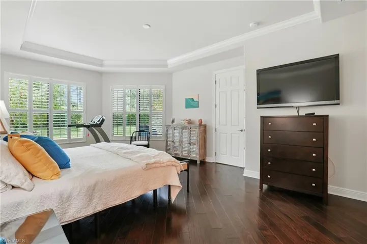 Bedroom with dark wood-style flooring, a tray ceiling, and crown molding