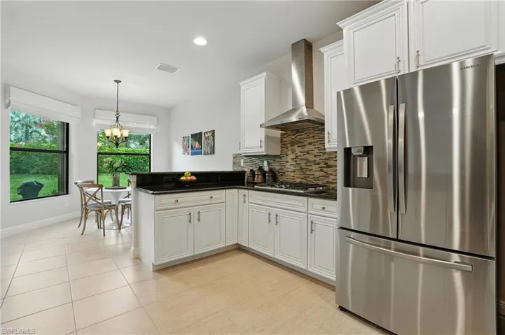 Kitchen with stainless steel appliances, wall chimney range hood, a peninsula, white cabinets, and backsplash