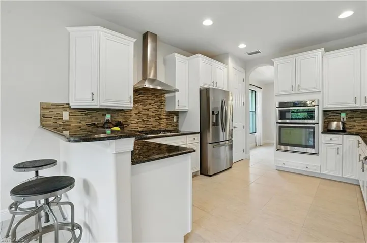 Kitchen with stainless steel appliances, wall chimney exhaust hood, arched walkways, a peninsula, and tasteful backsplash