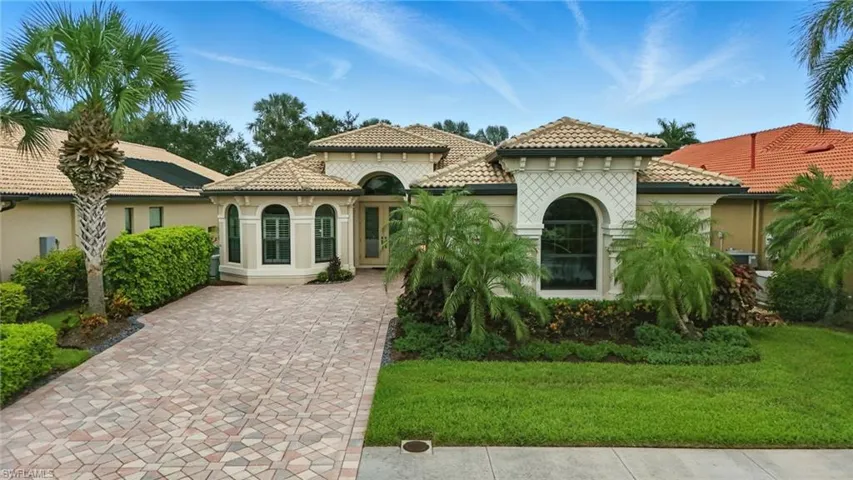 Mediterranean / spanish home with a tile roof, driveway, a front lawn, and stucco siding