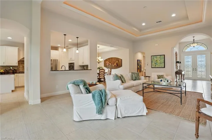 Living area featuring arched walkways, a raised ceiling, french doors, light tile patterned floors, and recessed lighting