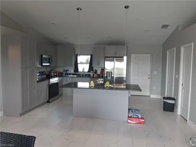 Kitchen featuring appliances with stainless steel finishes, decorative light fixtures, a center island, dark stone countertops, and gray cabinets