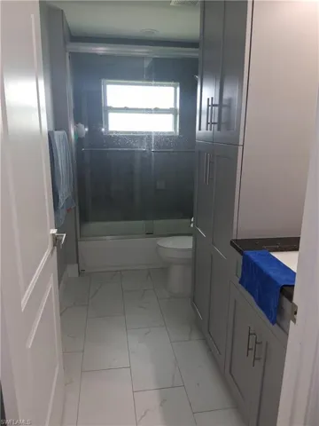 Bathroom with combined bath / shower with glass door, vanity, and light marble finish floors