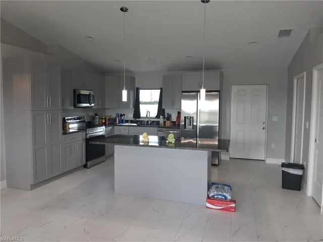 Kitchen featuring appliances with stainless steel finishes, gray cabinetry, hanging light fixtures, dark stone counters, and lofted ceiling