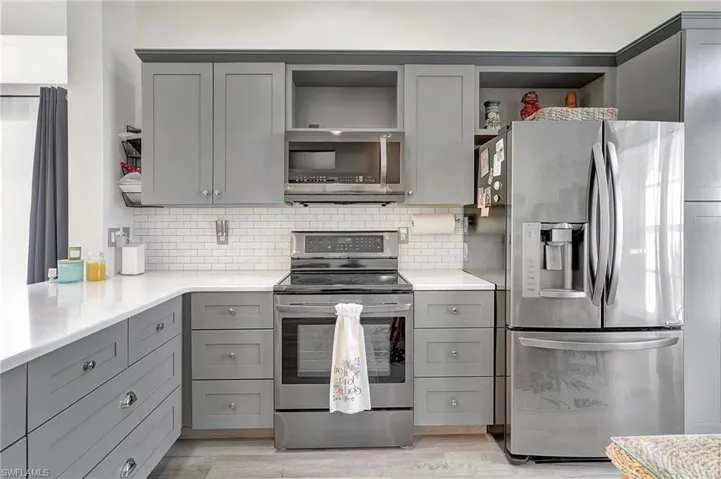 Kitchen featuring gray cabinets, appliances with stainless steel finishes, light hardwood / wood-style floors, and decorative backsplash