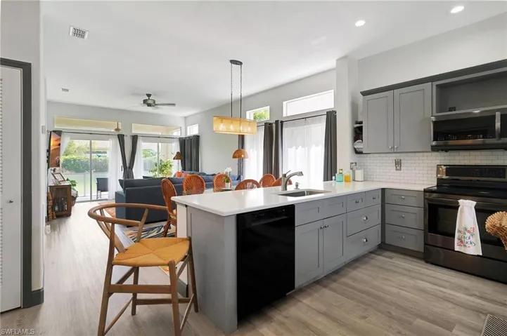 Kitchen with appliances with stainless steel finishes, gray cabinetry, kitchen peninsula, decorative light fixtures, and sink