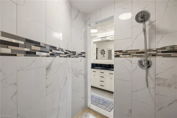 Bathroom featuring tiled shower, vanity, and tile walls