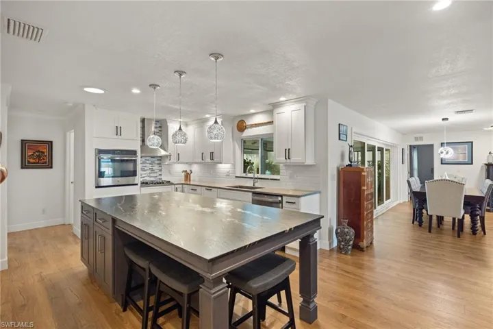 Kitchen featuring light hardwood / wood-style flooring, stainless steel appliances, wall chimney exhaust hood, and white cabinets