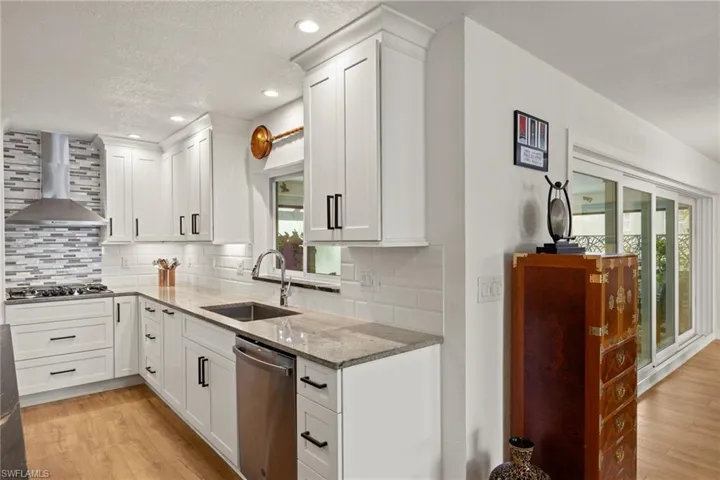 Kitchen with sink, light stone countertops, wall chimney exhaust hood, appliances with stainless steel finishes, and light hardwood / wood-style floors