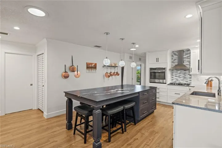 Kitchen featuring light wood-type flooring, sink, wall chimney exhaust hood, appliances with stainless steel finishes, and white cabinets